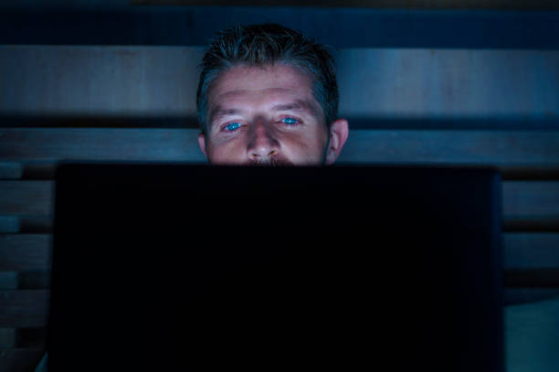 attrayant et détendue internet addict jeune réseau concentré tard dans la nuit sur le lit avec l’ordinateur portable dans le concept d’homme d’affaires de toxicomanie ou de bourreau de travail médias sociaux - addiction photos et images de collection