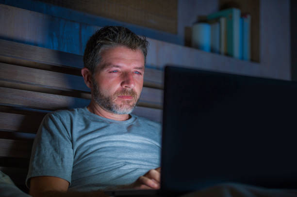 社会的なメディア中毒あるいはワーカホリック実業家の概念にラップトップ コンピューターが付いているベッドに夜遅く集中して魅力的で幸せなインターネット中毒の若者ネットワーク - internet addiction pornography computer ストックフォトと画像