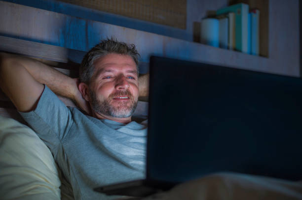 �매력적이 고 행복 한 인터넷 중독자 젊은이 네트워킹 소셜 미디어 중독 또는 중독 사업 개념에 노트북 컴퓨터와 함께 침대에 밤에 집중 - internet addiction pornography computer 뉴스 사진 이미지