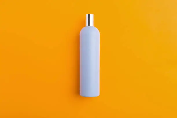 Empty blue plastic bottle lies on an orange background, the top view. Template