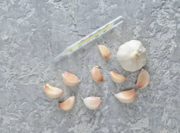 Photo of Garlic cloves and thermometer on a gray concrete surface. Traditional medicine against colds