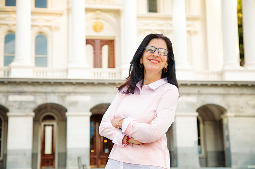 Hermoso retrato sonriente de mujer Latina de confianza media edad por edificio de gobierno photo