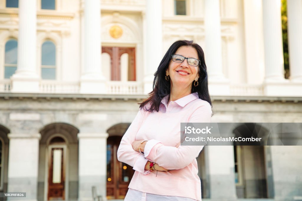 Confident Middle aged beautiful smiling Latina woman portrait by government building Confident Middle aged beautiful smiling Latina woman portrait by government building, arms crossed.. Civil Servant Stock Photo