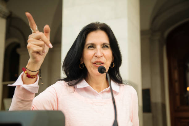 istock Mature Latina female politician points the way during speech over microphone 1083982948