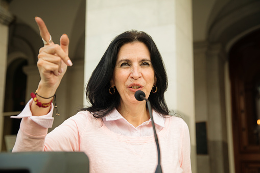 Mature Latina female politician points the way during public speech over microphone