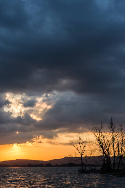 istock Beautiful sunset on a lake, with tree silhouettes and sun coming down under an overcast sky 1083987212