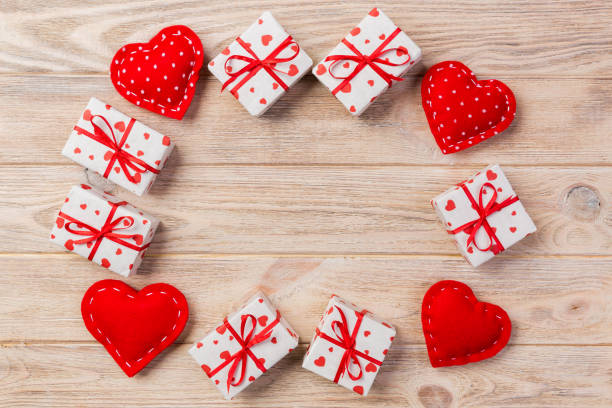 Valentine or other holiday handmade present in paper with red hearts and gifts box in holiday wrapper. Present box of gift on orange wooden table top view with copy space, empty space for design. san valentín u otro día de fiesta presente hecho a mano en papel con caja roja de corazones y regalos en la envoltura de vacaciones. presentar la caja de regalo en vista superior naranja de mesa de madera con espacio de copia, espacio vacío para el dise