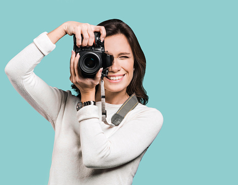 Beautiful girl photographer is taking pictures with dslr camera. Isolated on grey background