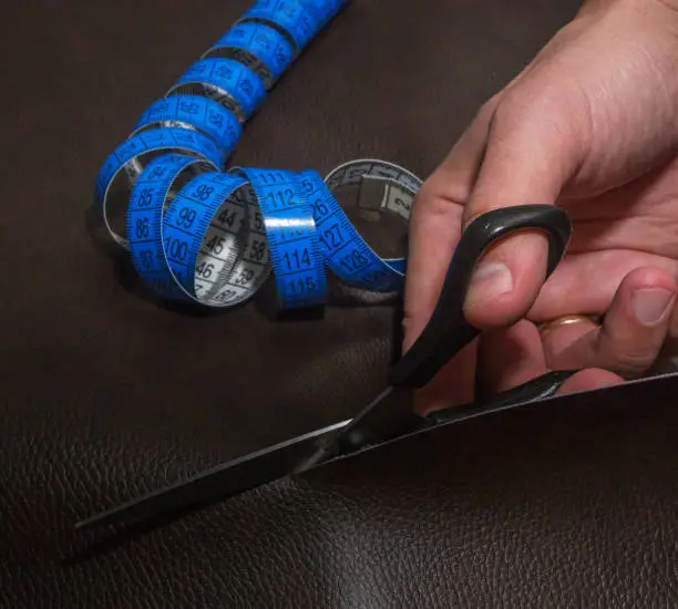 Leather cutting-out using black scissors and twisted blue tape measure, close-up