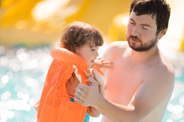 padre che aiuta la sua simpatica figlia bambino wuth il suo giubbotto di salvataggio nella piscina all'aperto nel parco acquatico (aquapark) - life jacket life belt buoy float foto e immagini stock