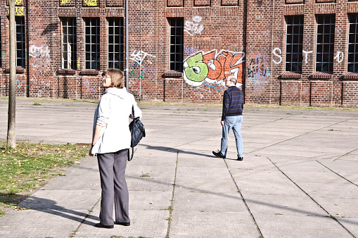 A couple admires Hochofenplatz - a decommissioned steel factory - while walking past a graffiti-covered brick wall in Phoenix West, Dortmund - Germany