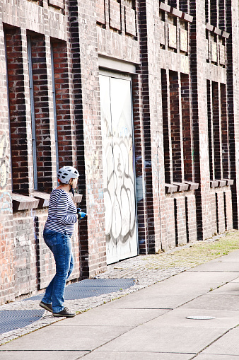 A female cyclist admiring Hochofenplatz - a decommissioned steel factory - and an old building with graffiti-covered brick wall in Phoenix West, Dortmund - Germany