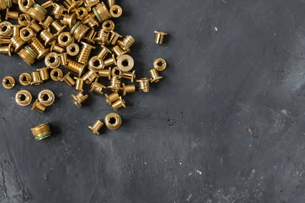 many metal gold threaded inserts made of lattin metal for making very hard connection between plastic details, oblong horizontal shot made from top view angle on the background of black rustic surface