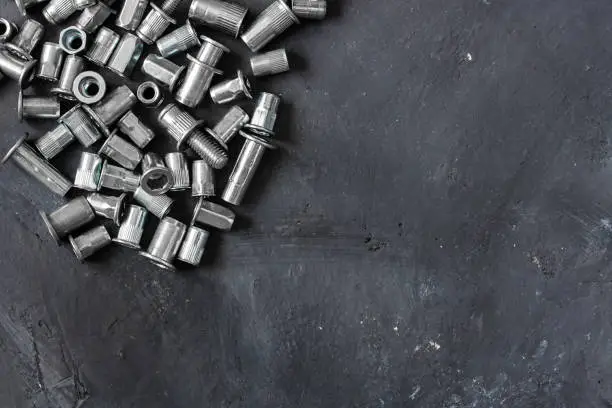 Many metal grey river nuts and clinch bolts on the upper left part of oblong horizontal shot made from the top view on the background of black rustic surface