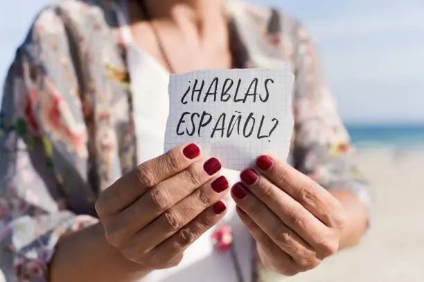 closeup of a caucasian woman outdoors showing a piece of paper with the question hablas espanol, do you speak spanish written in spanish