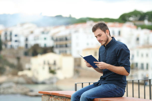 homem sério, lendo um livro de papel em uma cidade da costa - balcony beach book men - fotografias e filmes do acervo