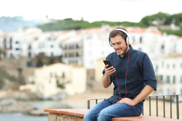 istock Happy man listening to music on a ledge in a town 1084046884