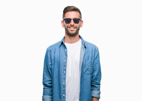 Young handsome man wearing sunglasses over isolated background with a happy and cool smile on face. Lucky person.