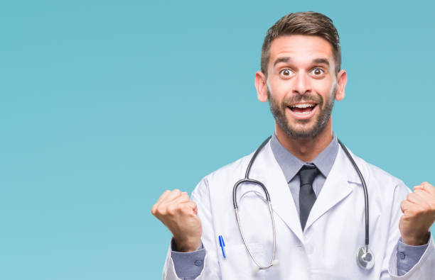 istock Young handsome doctor man over isolated background celebrating surprised and amazed for success with arms raised and open eyes. Winner concept. 1084051202