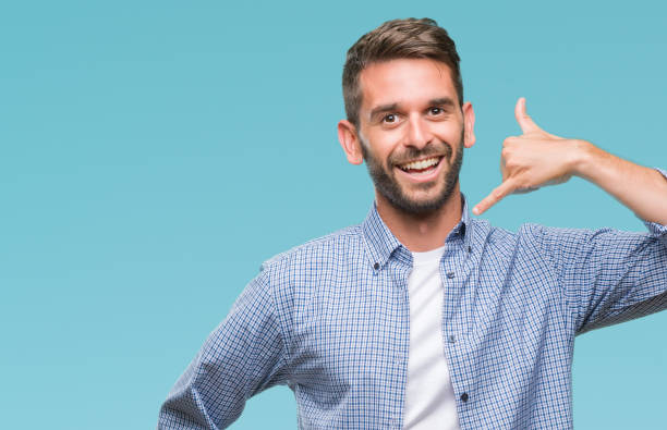 istock Young handsome man wearing white t-shirt over isolated background smiling doing phone gesture with hand and fingers like talking on the telephone. Communicating concepts. 1084051340