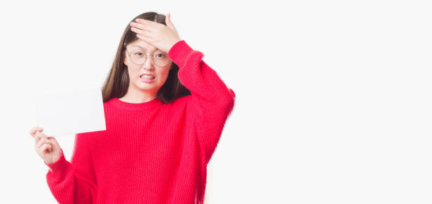 istock Young Chinese woman over isolated background holding blank card stressed with hand on head, shocked with shame and surprise face, angry and frustrated. Fear and upset for mistake. 1084057504