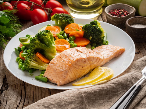 Steam salmon and vegetables, Paleo, keto, fodmap diet. White plate on old rustic wooden table, side view