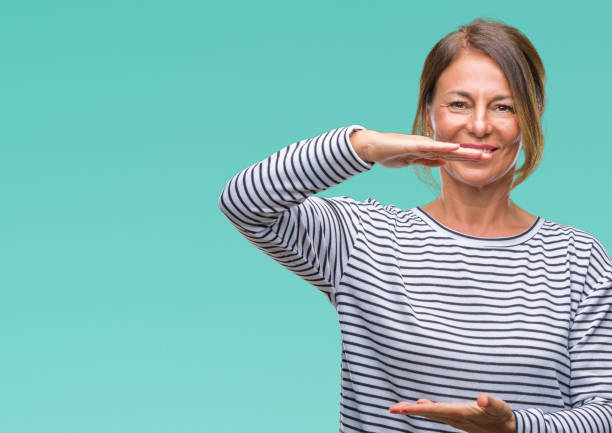 istock Middle age senior hispanic woman over isolated background gesturing with hands showing big and large size sign, measure symbol. Smiling looking at the camera. Measuring concept. 1084070802