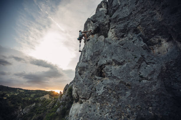 One man, disability young man with prosthetic leg free climbing on a rock in nature..