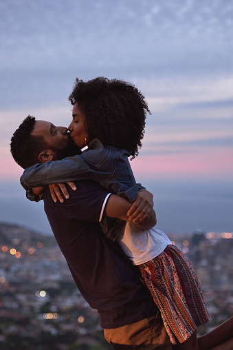 Young carefree romantic love affair, loving couple kissing at sunset with city lights