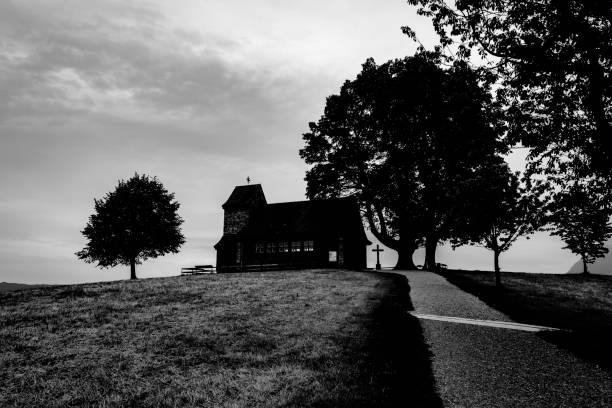 Empty road and small white chapel on a hill next to volcanic lake Weinfelder Maar ( Totenmaar ) in nature reserve in german Eifel region. Rhineland Palitanate, Germany. December 2015