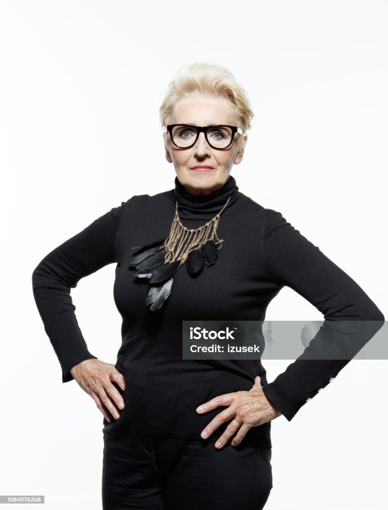 Portrait of bossy senior woman Glamour portrait of beautiful confident senior woman, wearing black clothes, glasses and jewelry. Standing with hands on hips and looking at camera. White Background Stock Photo
