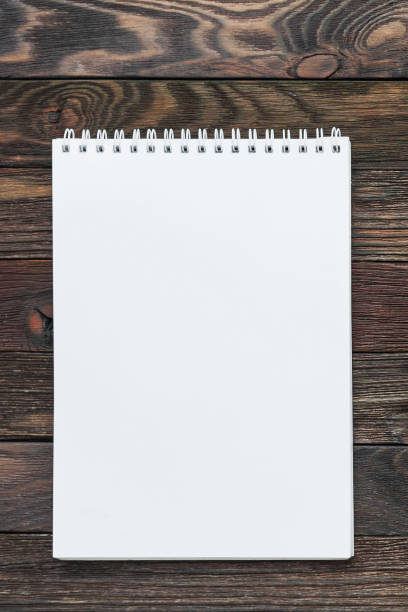 istock Wooden background with notepad. Clear white page may be used as mock up. Office supply for making notes or to do lists. 1084083740