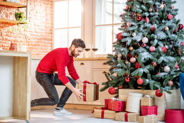 istock Man putting gifts under the New Year tree at home 1084086988