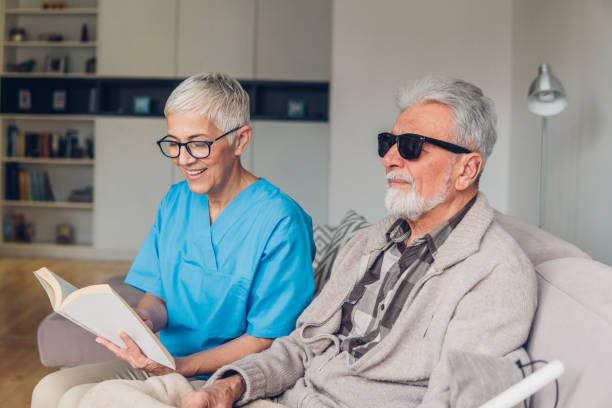 Happy woman reading to the blind Smiling female caregiver reading to blind patient blindness stock pictures, royalty-free photos & images