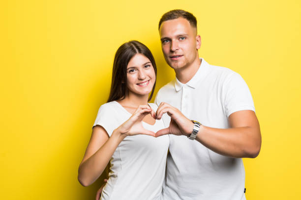 istock Young happy couple make heart with hands isolated on yellow background 1084091164
