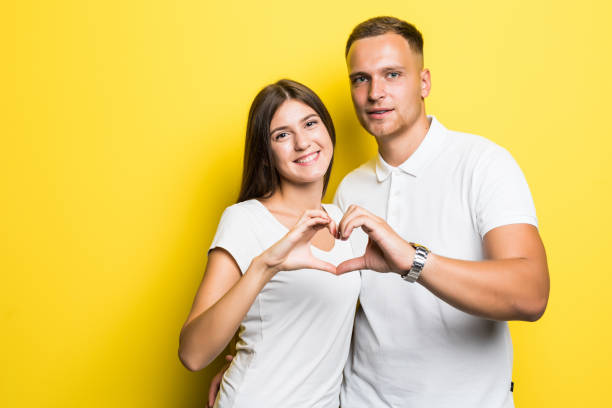 istock Young happy couple make heart with hands isolated on yellow background 1084092696