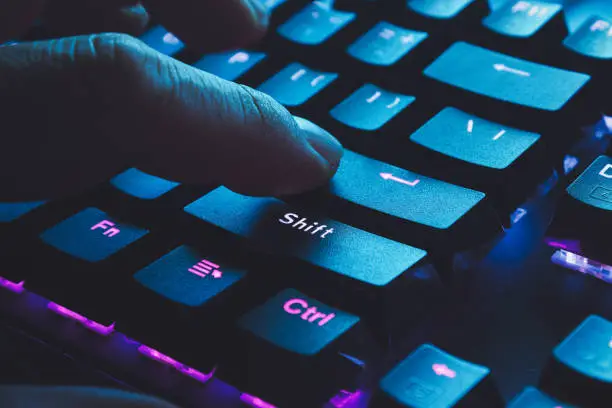 Photo of Male hand typing on the black illuminated  keyboard with blue light coming from screen