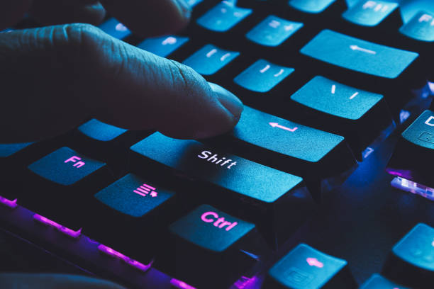 mão masculina, digitar no teclado iluminado preto com luz azul proveniente de tela - enter key - fotografias e filmes do acervo
