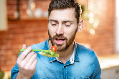 Close-up portrait of a handsome man eating healthy salad on the kitchen at home