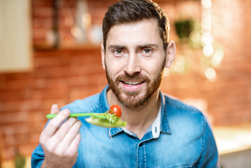 Close-up portrait of a handsome man eating healthy salad on the kitchen at home