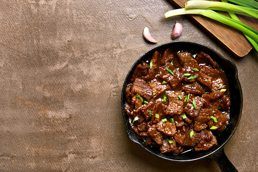 Beef stewed in soy sauce with spices in asian style on brown background with copy space. Mongolian beef. Top view, flat lay