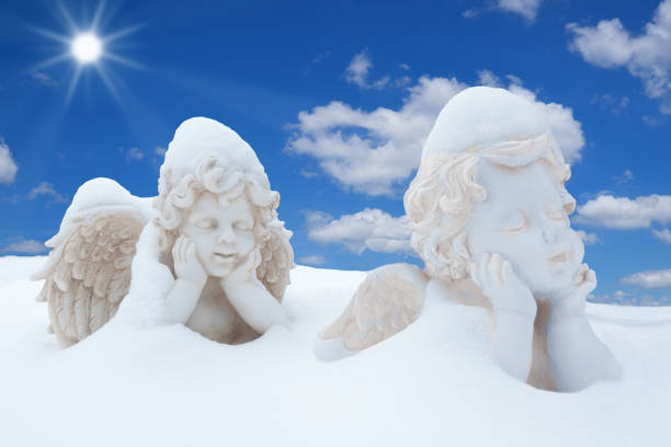 Two snowy angels with propped arms against blue and white sky with sun