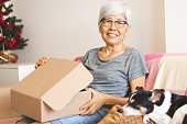 高齢者のアジア女性とオンラインでの購入から配信されたパーセルを開く彼女の怠惰な犬