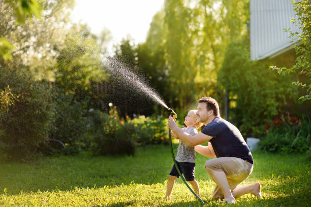 lustige kleine junge mit seinem vater spielt mit gartenschlauch in sonnigen hinterhof - schlauch stock-fotos und bilder