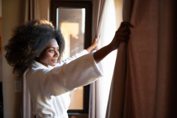 donna che tira tende in camera d'albergo - bathrobe foto e immagini stock