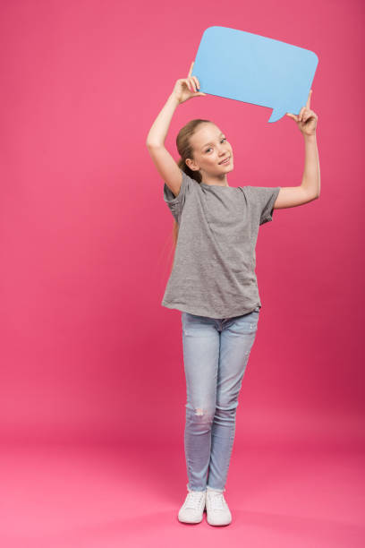 istock smiling preteen kid holding blue speech bubble, isolated on pink 1084108532