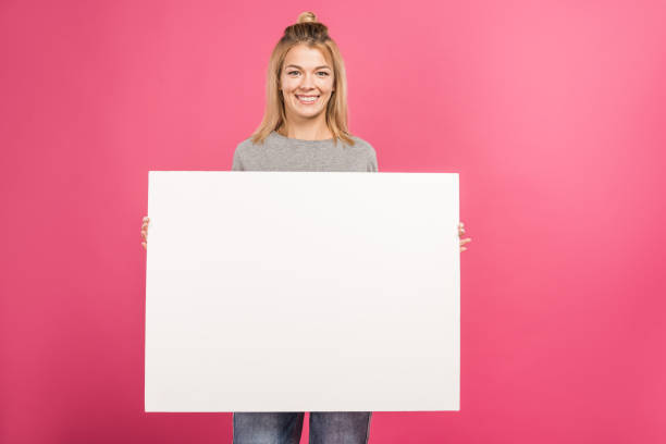 istock attractive woman holding empty board, isolated on pink 1084108608