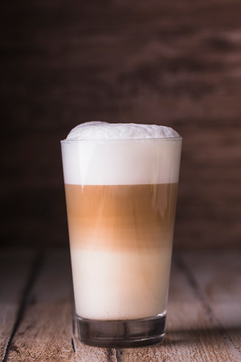 Coffee cafe latte macchiato in a high glass on a wooden background. There is copy space next to the glass, and the photo is horizontal.