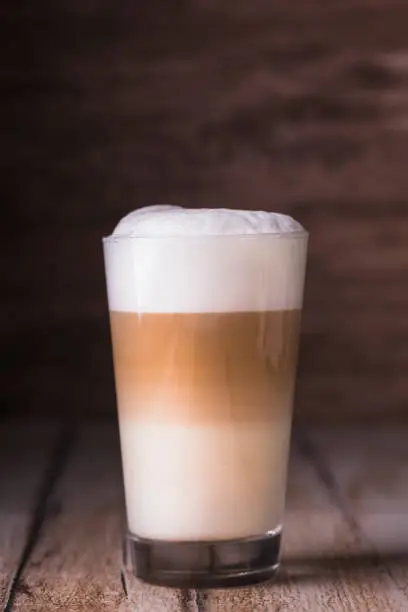 Coffee cafe latte macchiato in a high glass on a wooden background. There is copy space next to the glass, and the photo is horizontal.