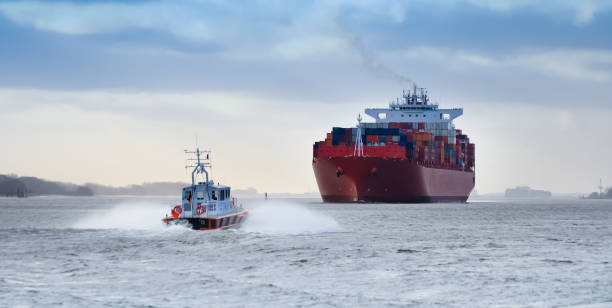 ein kleines lotsenboot vor einem riesigen containerschiff auf dem fluss elbe, deutschland - tugboat stock-fotos und bilder